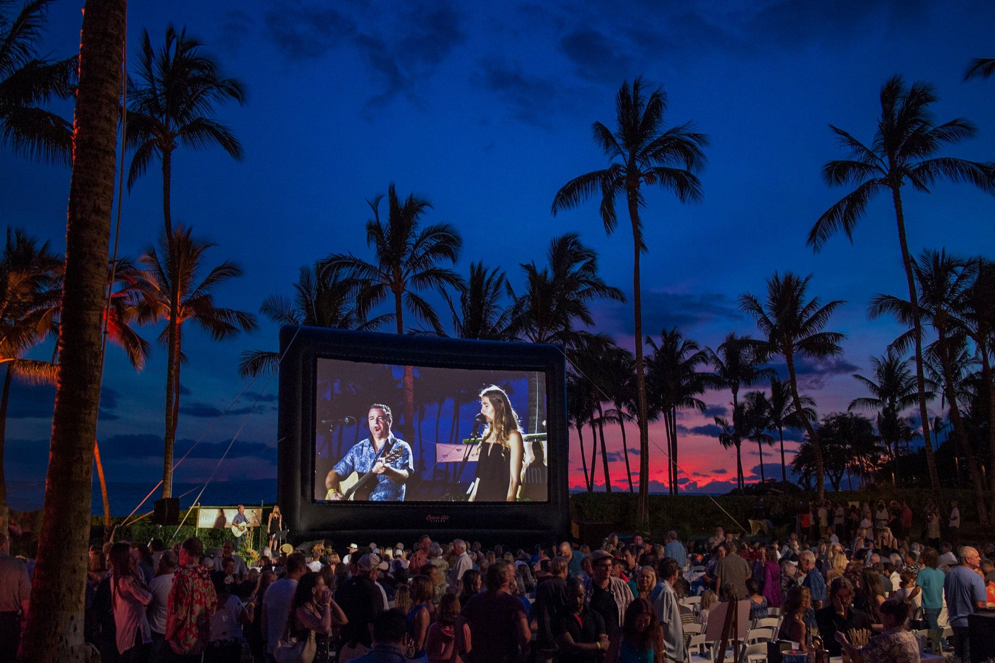 Зрители уличного кинопоказа собрались перед надувным экраном Open Air Cinema в сумерках